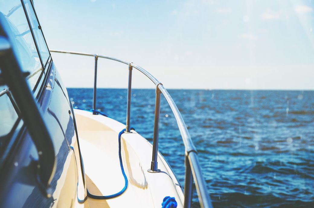 The image captures a close-up view of a boat's railing against a serene ocean backdrop. The clear blue sky reflects off the water's surface, suggesting a calm day at sea. — Credit: Photo by Austin Neill on Unsplash