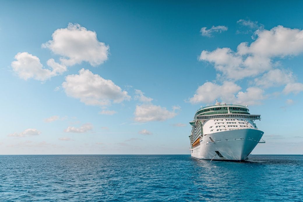 A large cruise ship is anchored in calm blue waters under a clear sky with a few scattered clouds. The ship's bow is prominently visible, showcasing its size and design as it floats peacefully at sea. — Credit: Photo by Josiah Weiss on Unsplash