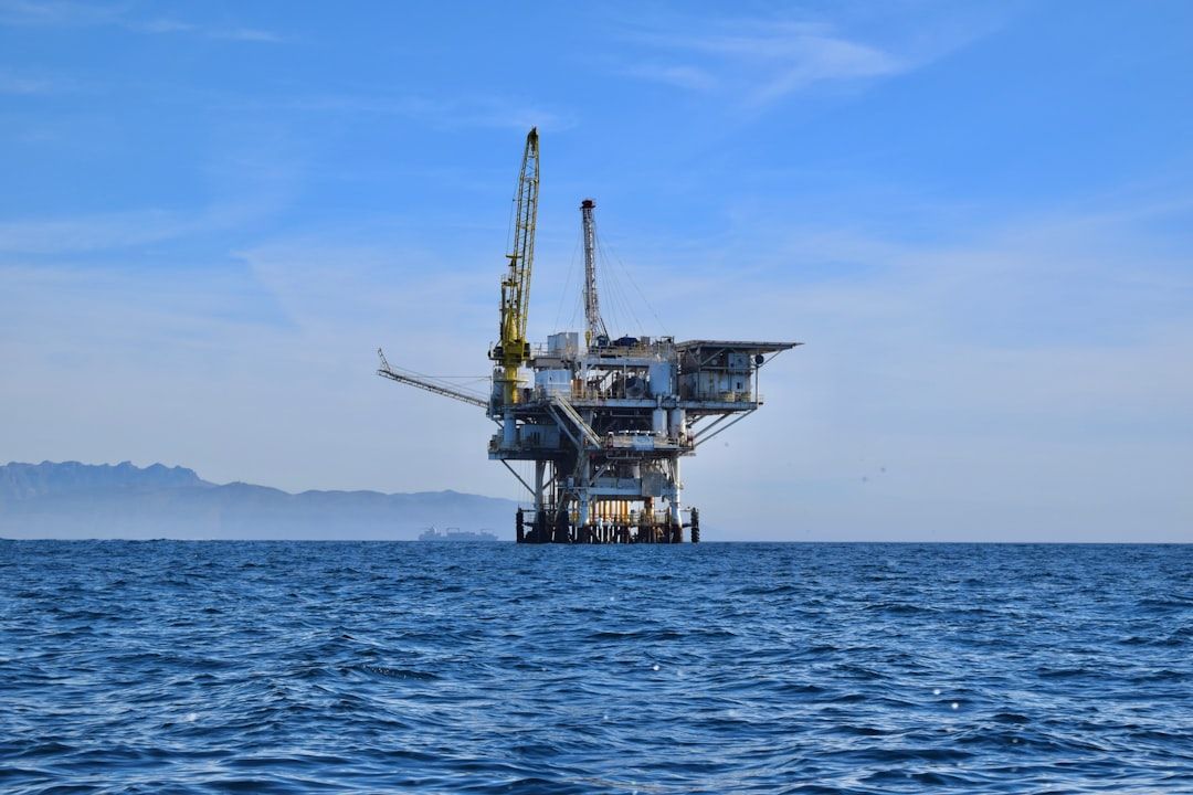An offshore oil rig stands prominently in the ocean against a clear sky. The structure features cranes and multiple platforms, indicating active extraction operations.