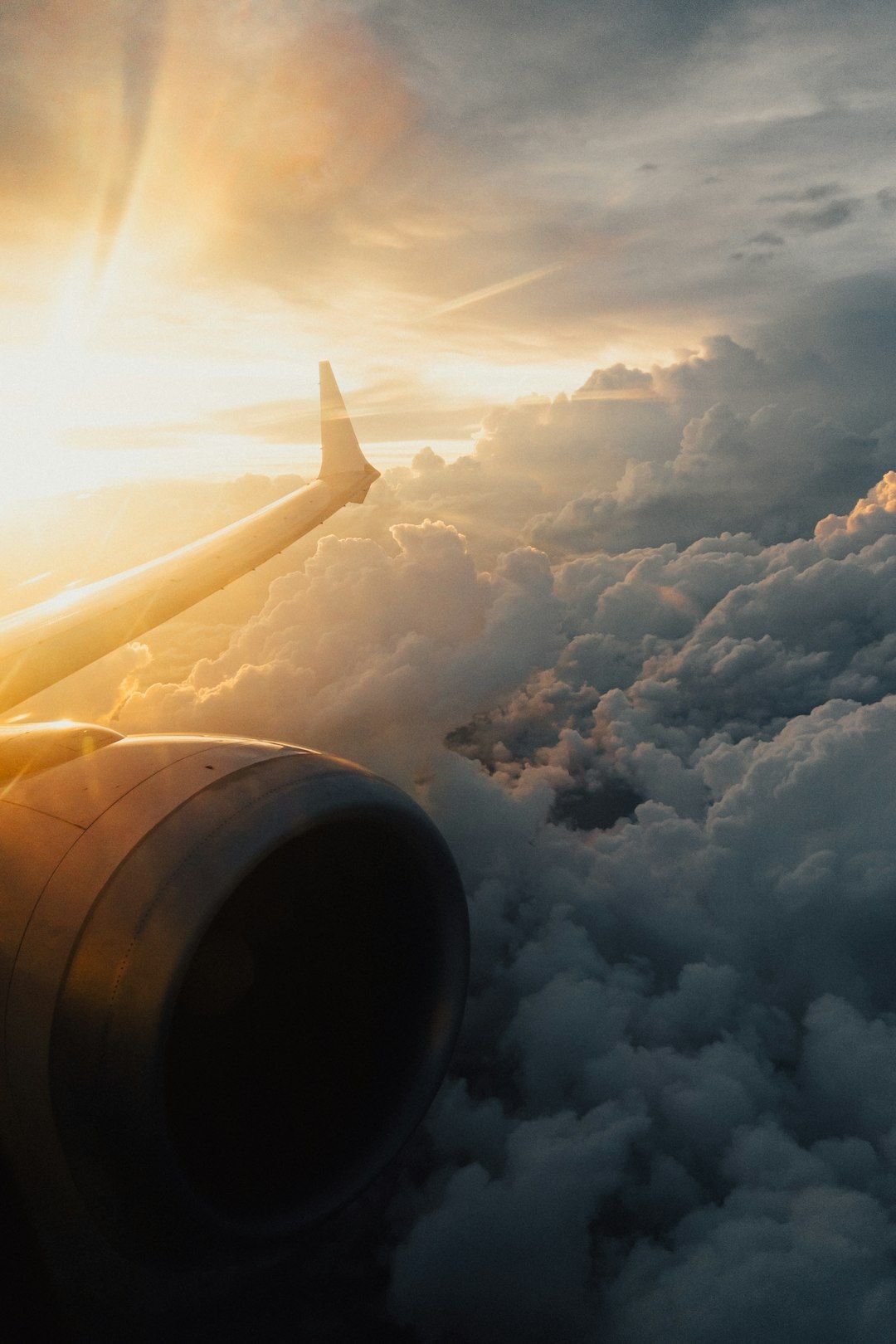 An airplane wing extends out over a dramatic cloudscape, bathed in golden sunset light. The image captures a serene yet awe-inspiring aerial view, showcasing the calmness of flying above the clouds.