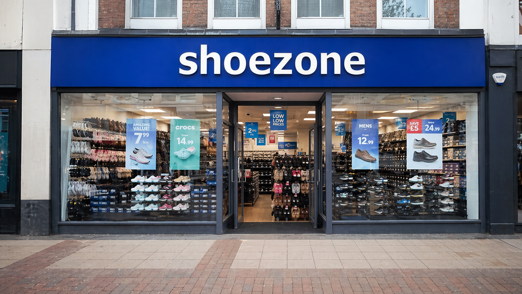 A retail shoe store named 'shoezone' located on a city street. The storefront features displays of various shoe styles and price tags visible through large glass windows.