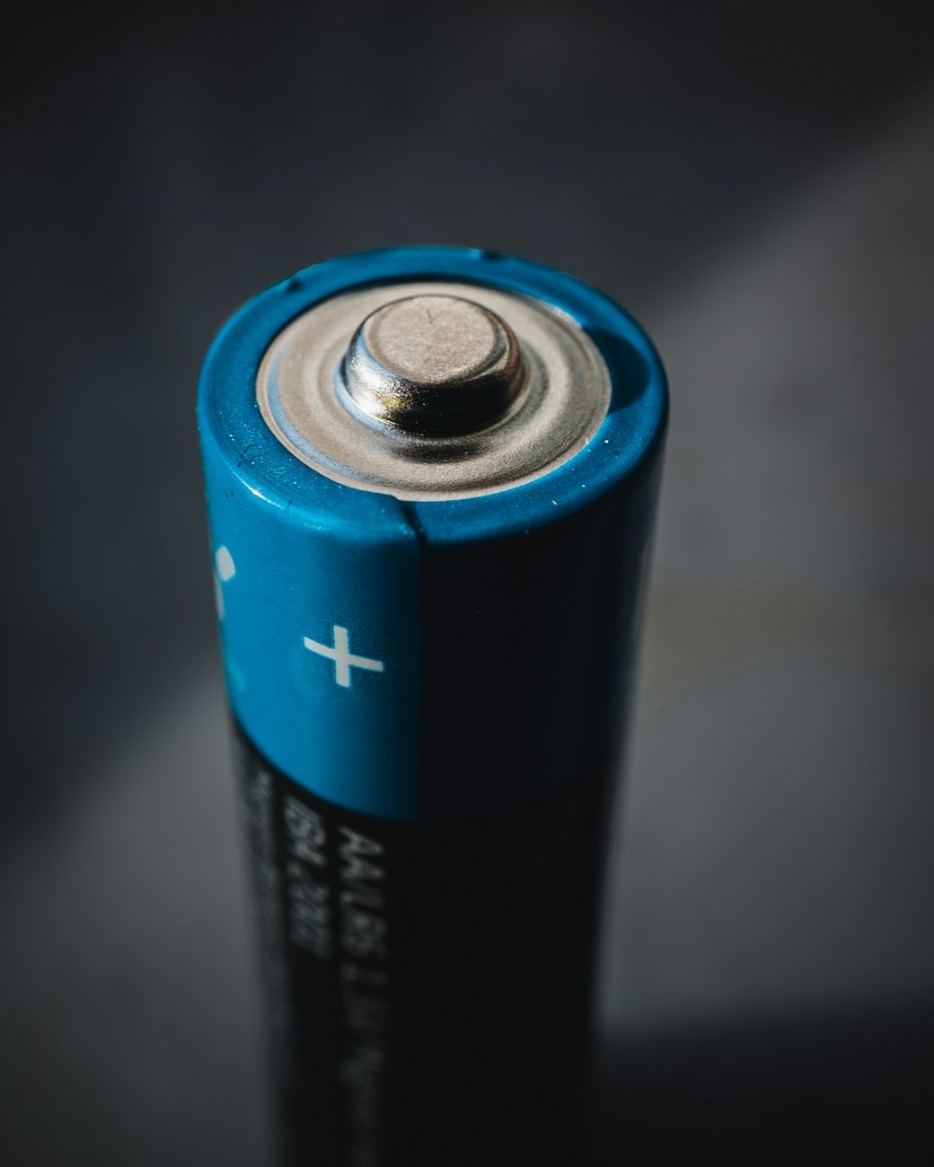 The image features a close-up of a blue AA battery, showcasing its top end with a visible positive terminal. The background is softly blurred, emphasizing the battery's design and details. — Credit: Photo by Mika Baumeister on Unsplash