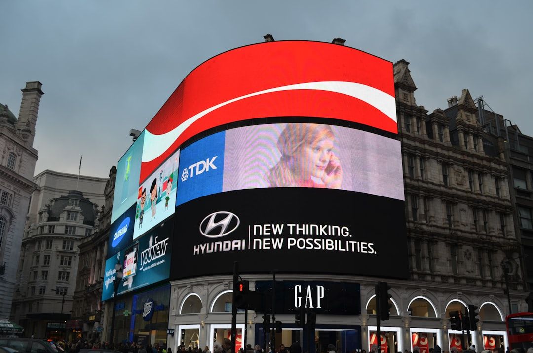 The image showcases a vibrant urban scene with large digital billboards displaying advertisements. Prominent brands such as Hyundai and TDK are featured, along with other advertisements, in a lively commercial area.
