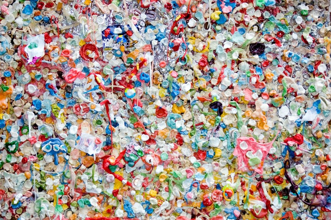 The image depicts a vibrant wall covered in a multitude of colorful chewing gum pieces, creating a chaotic but artistic visual texture. The various hues and textures of the gum create an abstract, almost mosaic-like appearance.