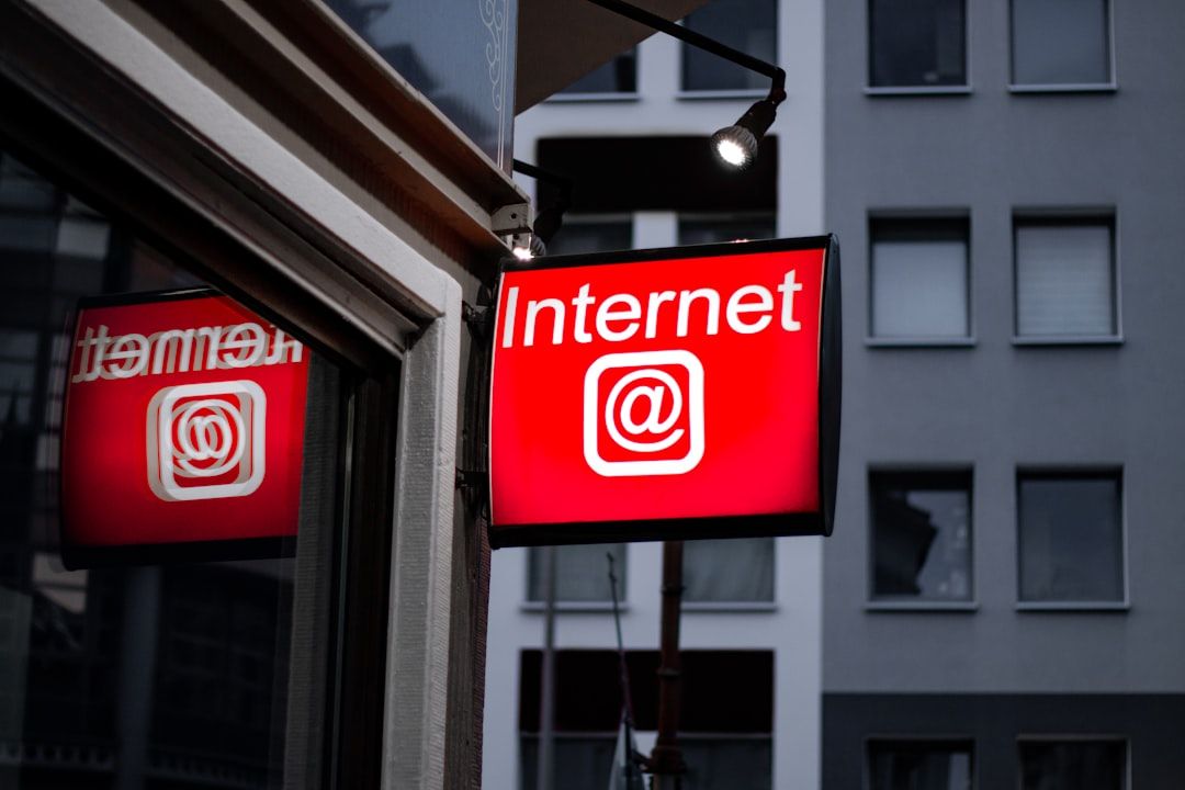 A brightly lit sign displaying the word 'Internet' accompanied by an '@' symbol. The sign is mounted on a building exterior, reflecting urban architecture in the background.