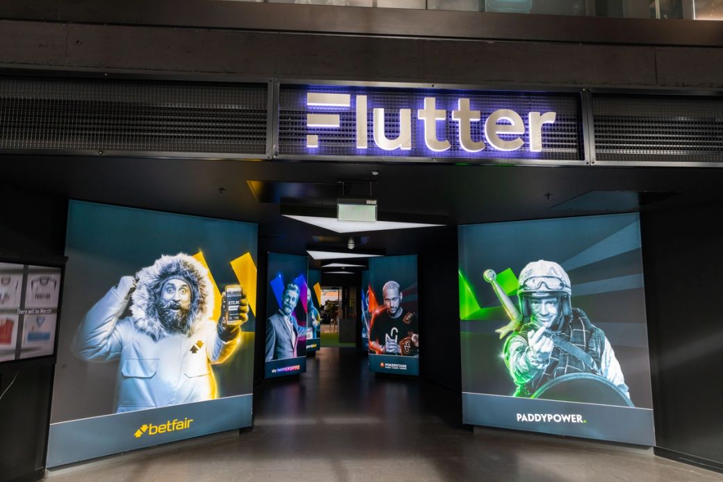 The image shows the entrance of a gambling facility featuring digital displays on either side. One display features a person in winter clothing holding a mobile device, while the other depicts a soldier in tactical gear, suggesting a playful and engaging atmosphere.