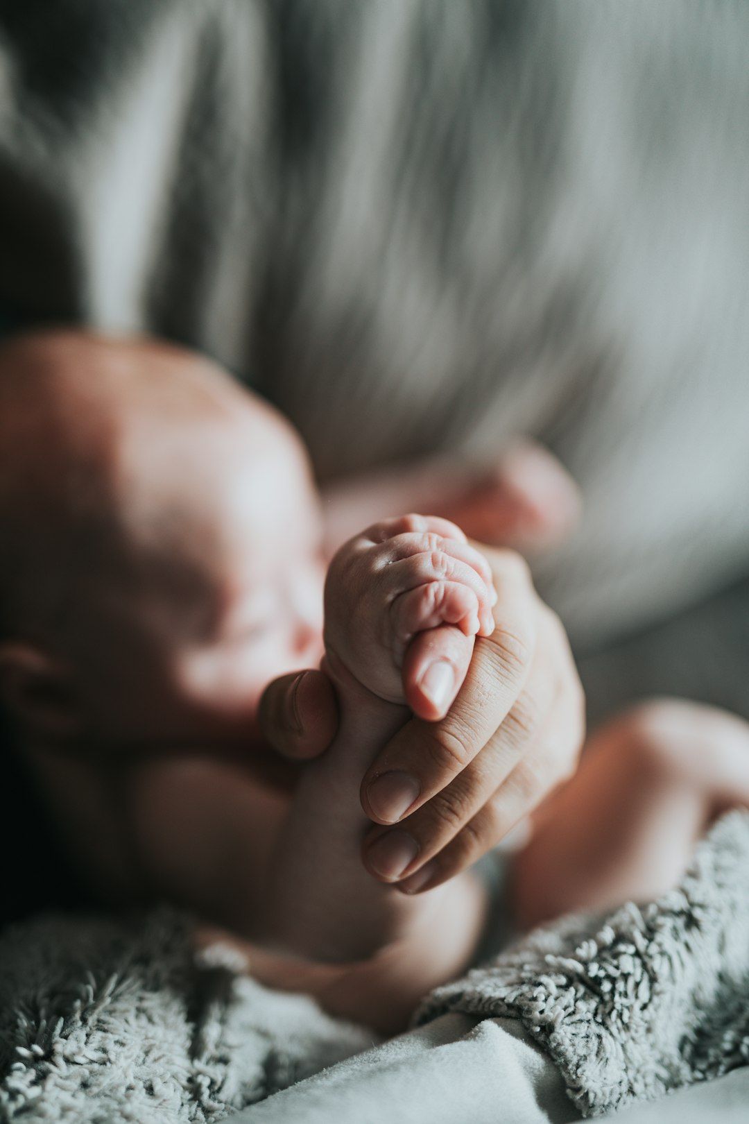 A close-up image depicting a caregiver gently holding a newborn's hand. The soft focus creates a warm and nurturing atmosphere, emphasizing the bond between the two individuals.