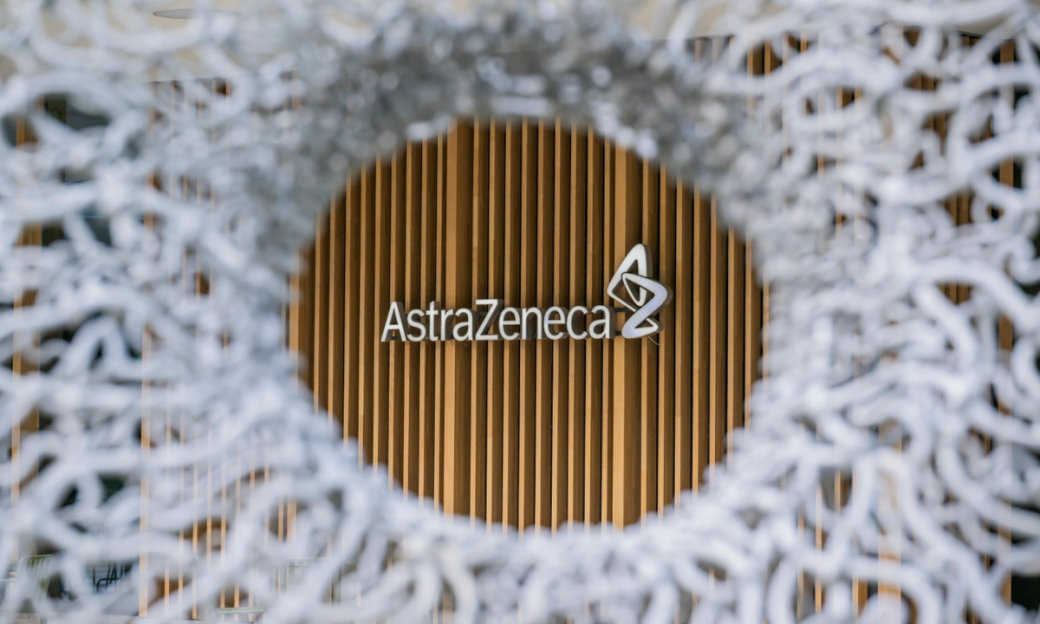The image features the AstraZeneca logo prominently displayed against a backdrop of wooden paneling. The logo is framed by a decorative circular design, emphasizing the branding of the pharmaceutical company. — Credit: Anthony Devlin/Getty Images for AstraZeneca