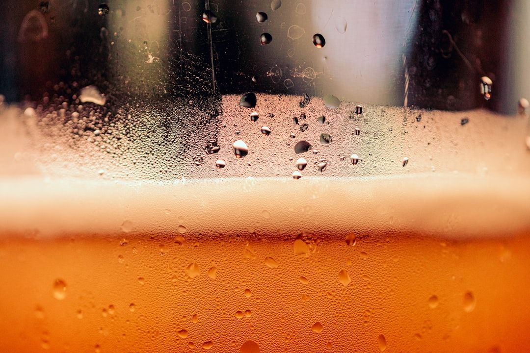 The image features a close-up view of a glass of beer, showcasing condensation on the outer surface. The amber hue of the beer is visible beneath the frothy head, creating a refreshing appearance.