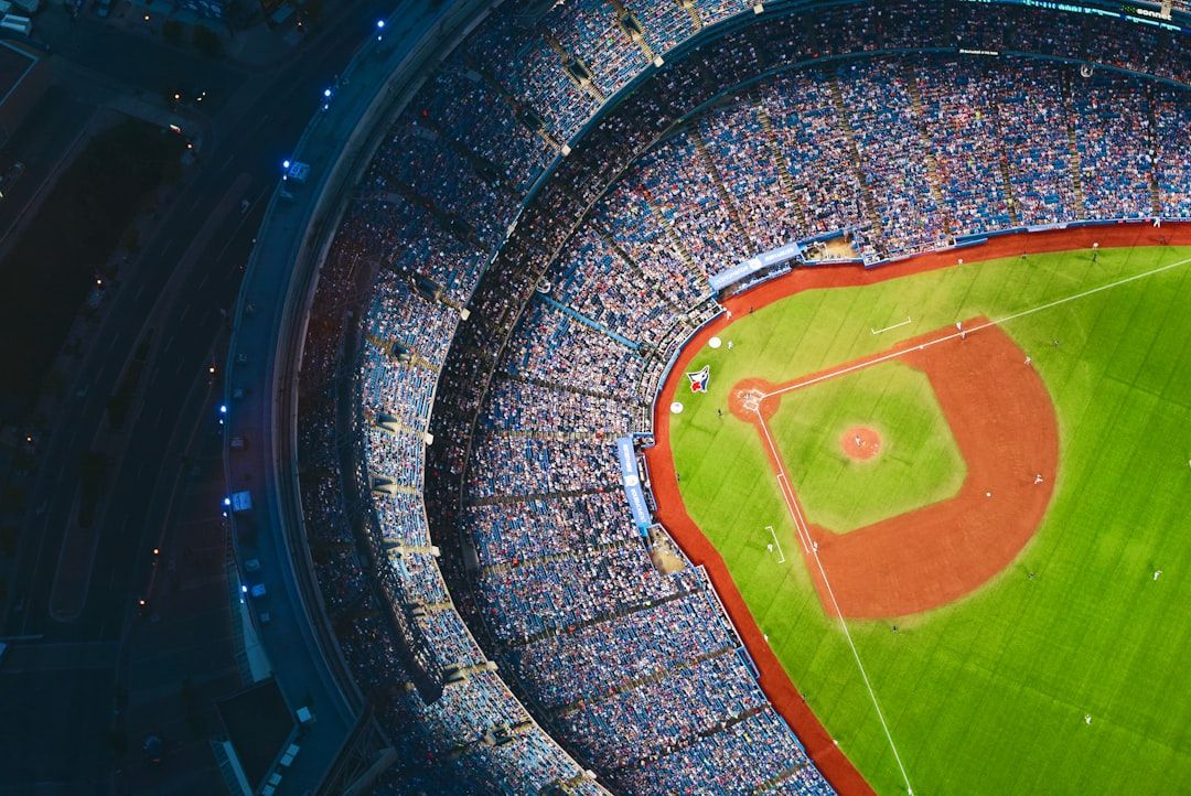 An aerial view of a packed baseball stadium during a game, showcasing the vibrant green field, the pitcher's mound, and the bases. The stands are filled with spectators, creating a lively atmosphere.