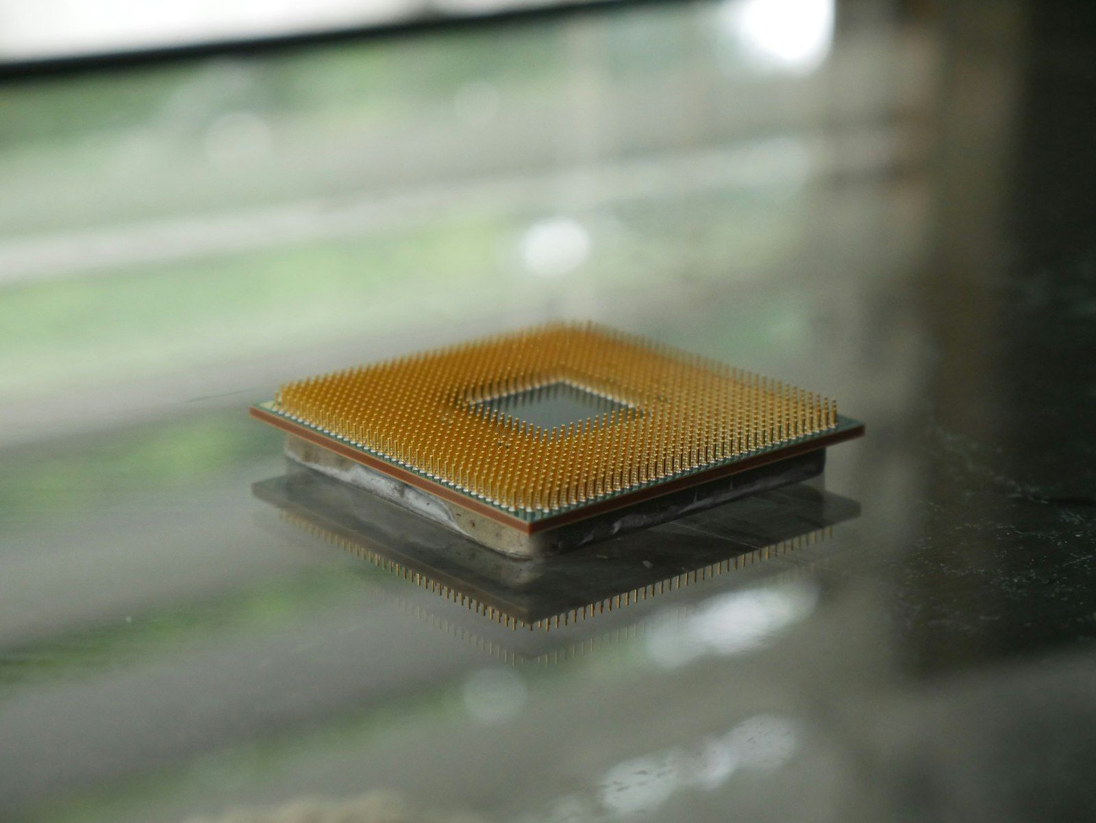 The image features a close-up view of a computer microprocessor resting on a reflective surface. The processor showcases a grid of gold pins and a square shape, highlighting its intricate design.