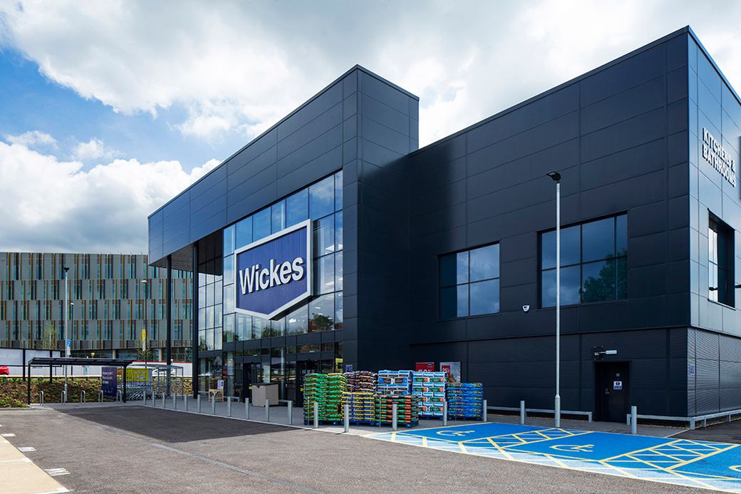 The image shows a modern retail building with a prominent branded sign. The exterior features a sleek design and is surrounded by a parking lot with distinct marked spaces.