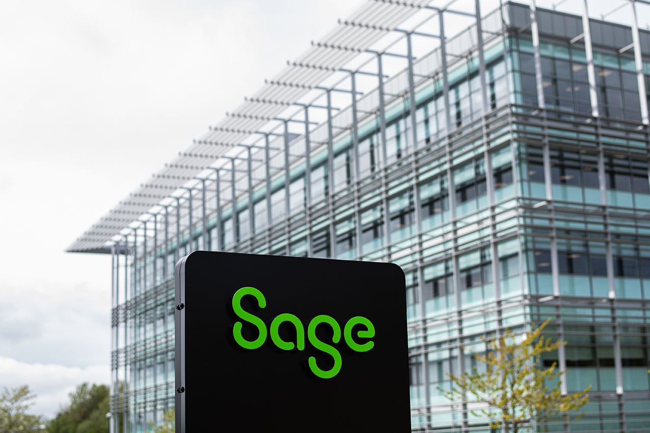 The image features a modern office building with a prominent sign that reads 'Sage' in green lettering. The structure showcases a contemporary architectural design with glass elements and metal framework.