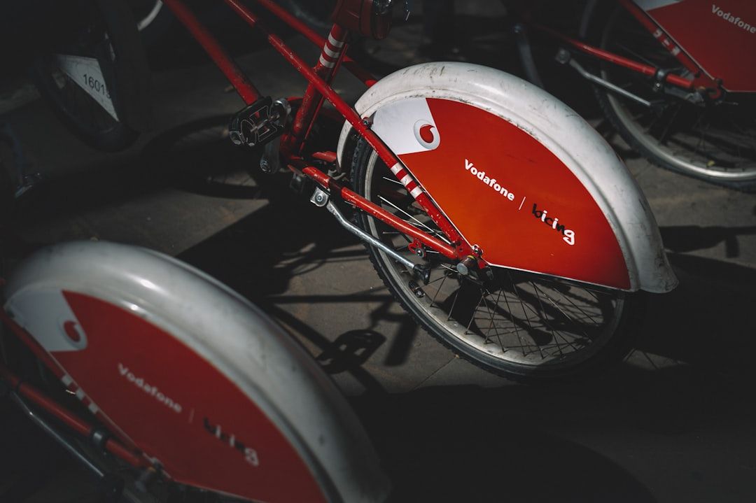The image shows a close-up view of red bicycles parked, featuring distinctive large white fenders. One of the fenders has a visible brand logo, indicating a connection to a telecommunications company.