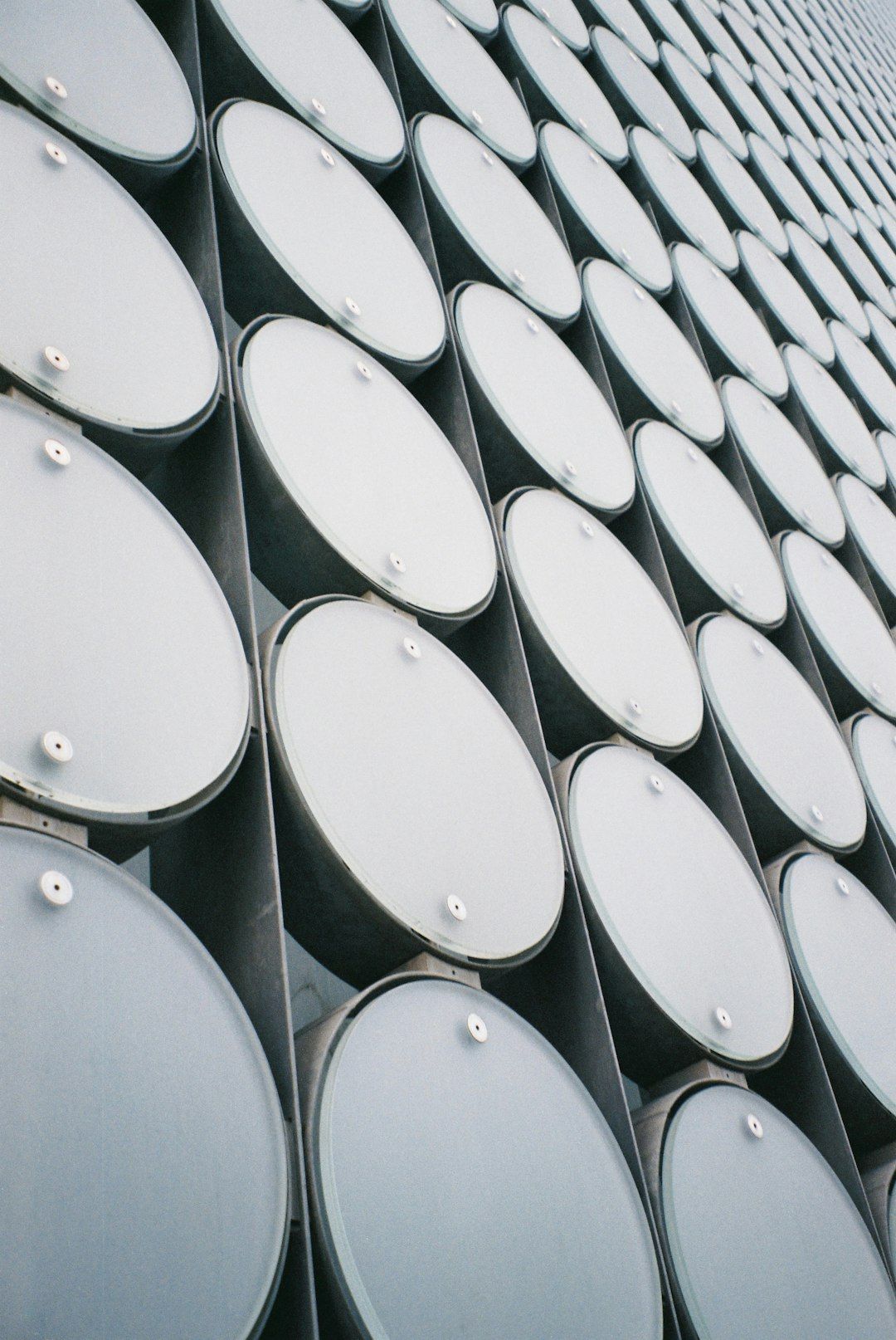 The image features an abstract close-up of a modern building facade, showcasing a series of cylindrical structures arranged in a grid-like pattern. The repetition and uniformity of the design create a visually striking effect.