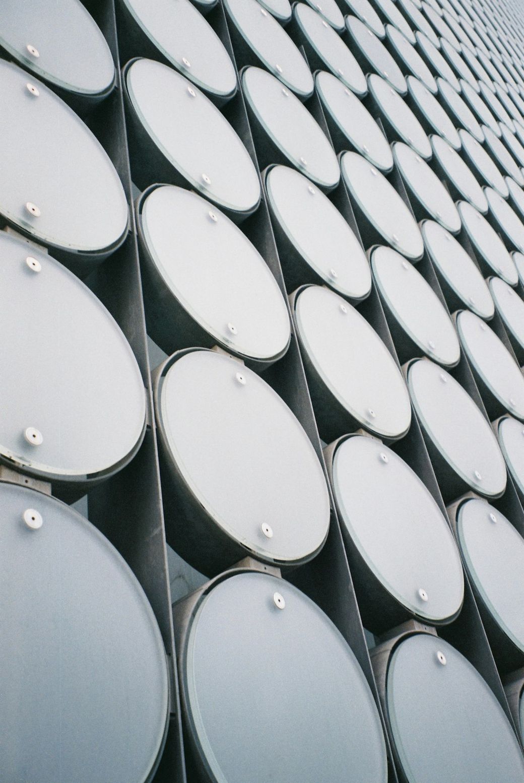 The image features an abstract close-up of a modern building facade, showcasing a series of cylindrical structures arranged in a grid-like pattern. The repetition and uniformity of the design create a visually striking effect. — Credit: Photo by Ben Tofan on Unsplash