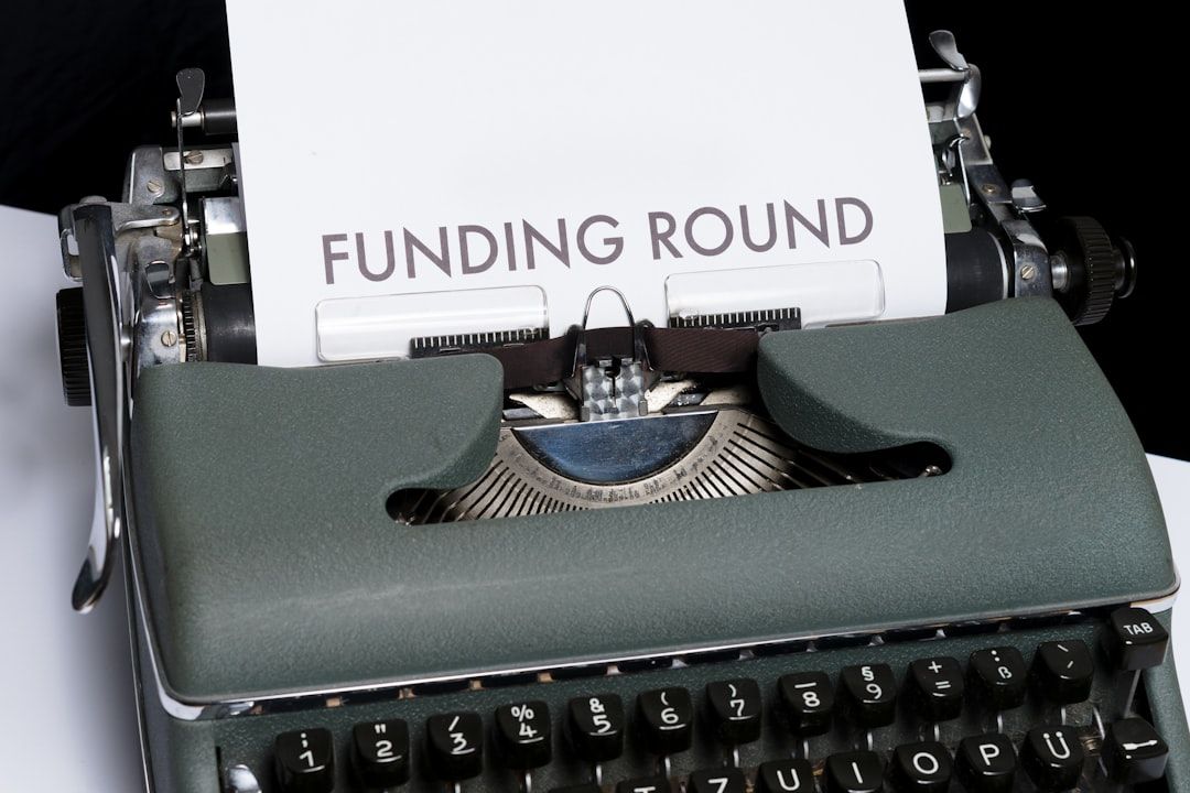 This image features a vintage typewriter with a sheet of paper inserted, displaying the text 'FUNDING ROUND'. The typewriter is positioned on a white surface, emphasizing its retro design.