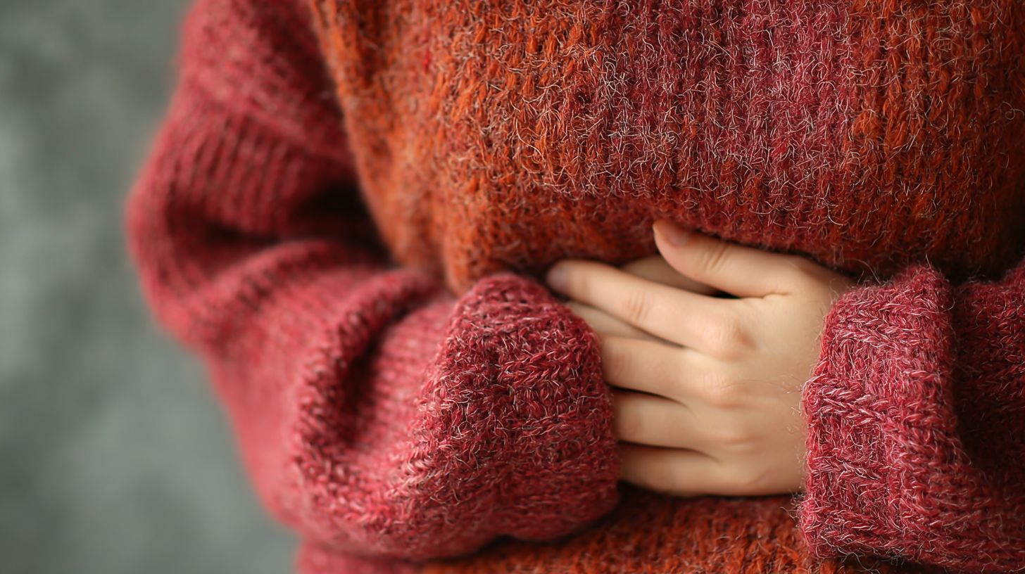 The image features a close-up of a person wearing a cozy, knitted sweater, with their hands resting on their stomach. The texture of the sweater and the warm colors create an inviting and comfortable atmosphere. Also related to stomach ache, IBS and digestion issues.