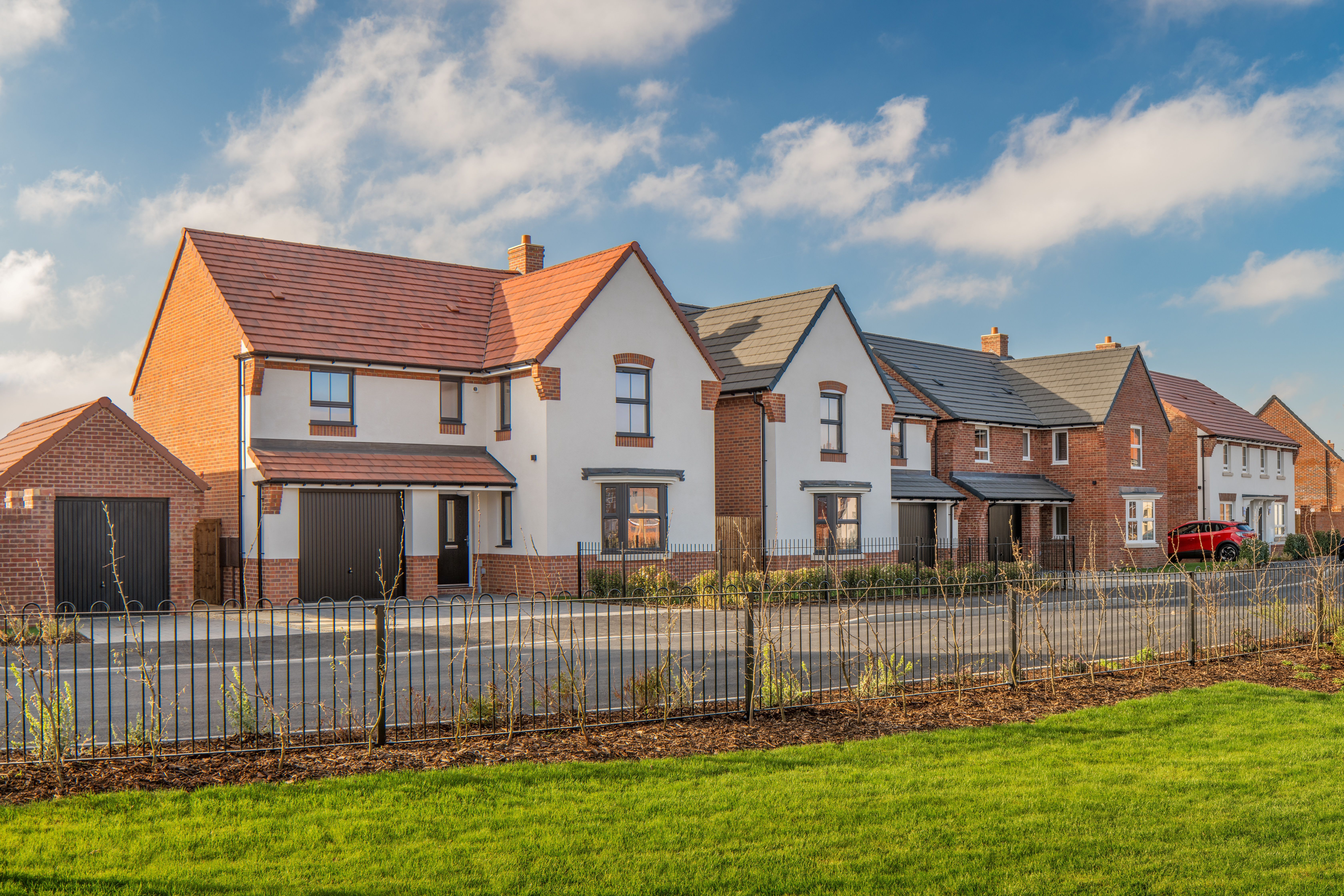 A row of newly constructed residential houses is depicted, showcasing modern architectural styles. The scene is set in a suburban area, featuring manicured lawns and a clear blue sky.