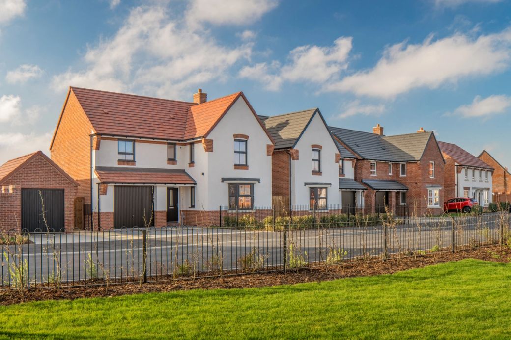 A row of newly constructed residential houses is depicted, showcasing modern architectural styles. The scene is set in a suburban area, featuring manicured lawns and a clear blue sky.