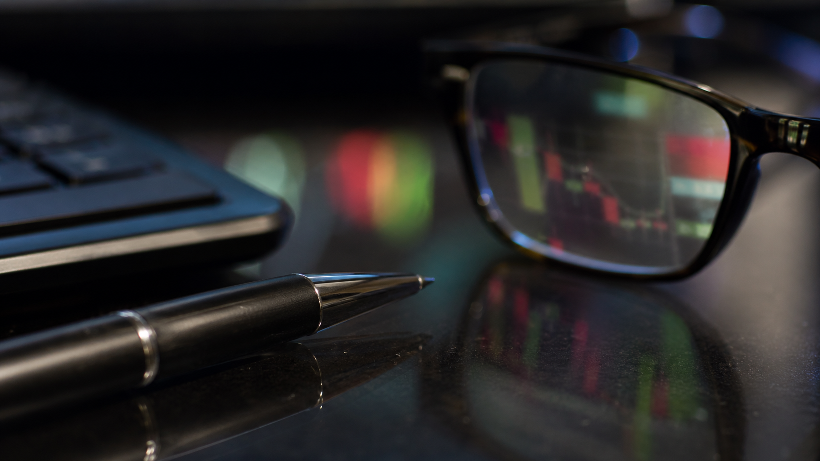 The image features a close-up of eyeglasses reflecting stock market data on a desk alongside a pen and a keyboard. The colorful charts displayed in the lenses suggest a focus on financial analysis or trading.