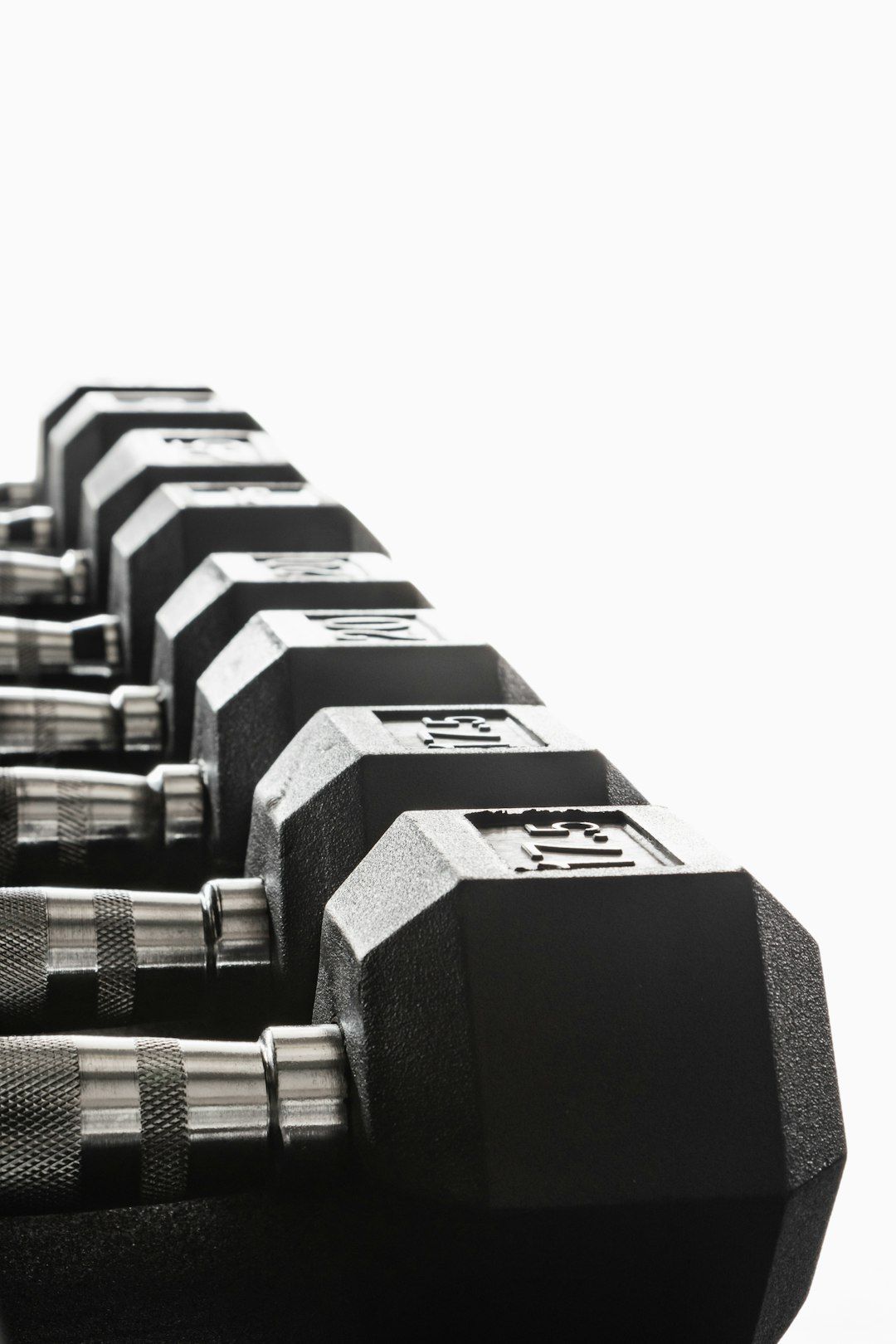 A close-up view of a set of black dumbbells arranged in a row. The dumbbells are made of metal with a textured grip and clearly display their weights.