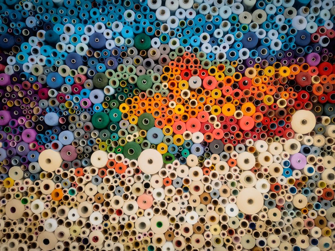 The image showcases a vibrant arrangement of colorful spools and threads arranged in a visually striking pattern. The various colors and sizes create a dynamic mosaic effect, highlighting the artistic potential of textile materials.