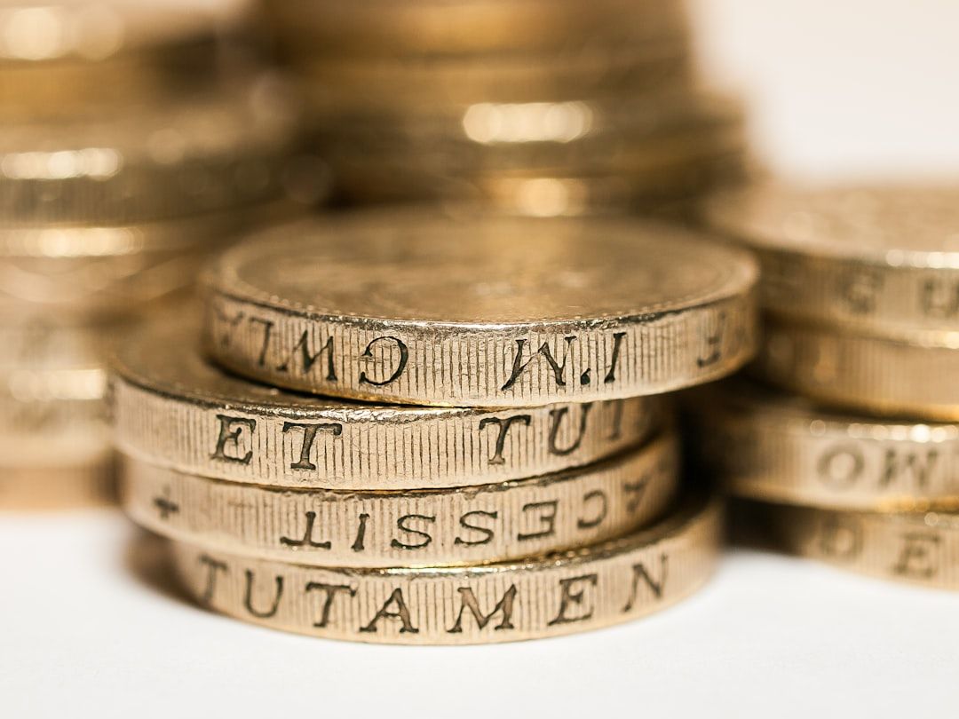 The image features a close-up of stacked coins, showcasing their intricate engravings and metallic sheen. The coins appear to be British pounds, highlighting various inscriptions.