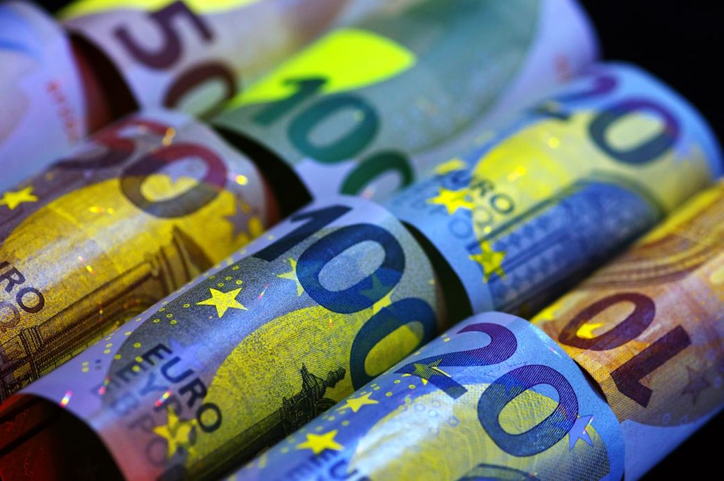 A close-up image of various Euro banknotes arranged in a row. The denominations visible include 20, 50, 100, and 200 Euros, showcasing the colorful designs and intricate details of the currency. — Credit: Photo by Immo Wegmann on Unsplash