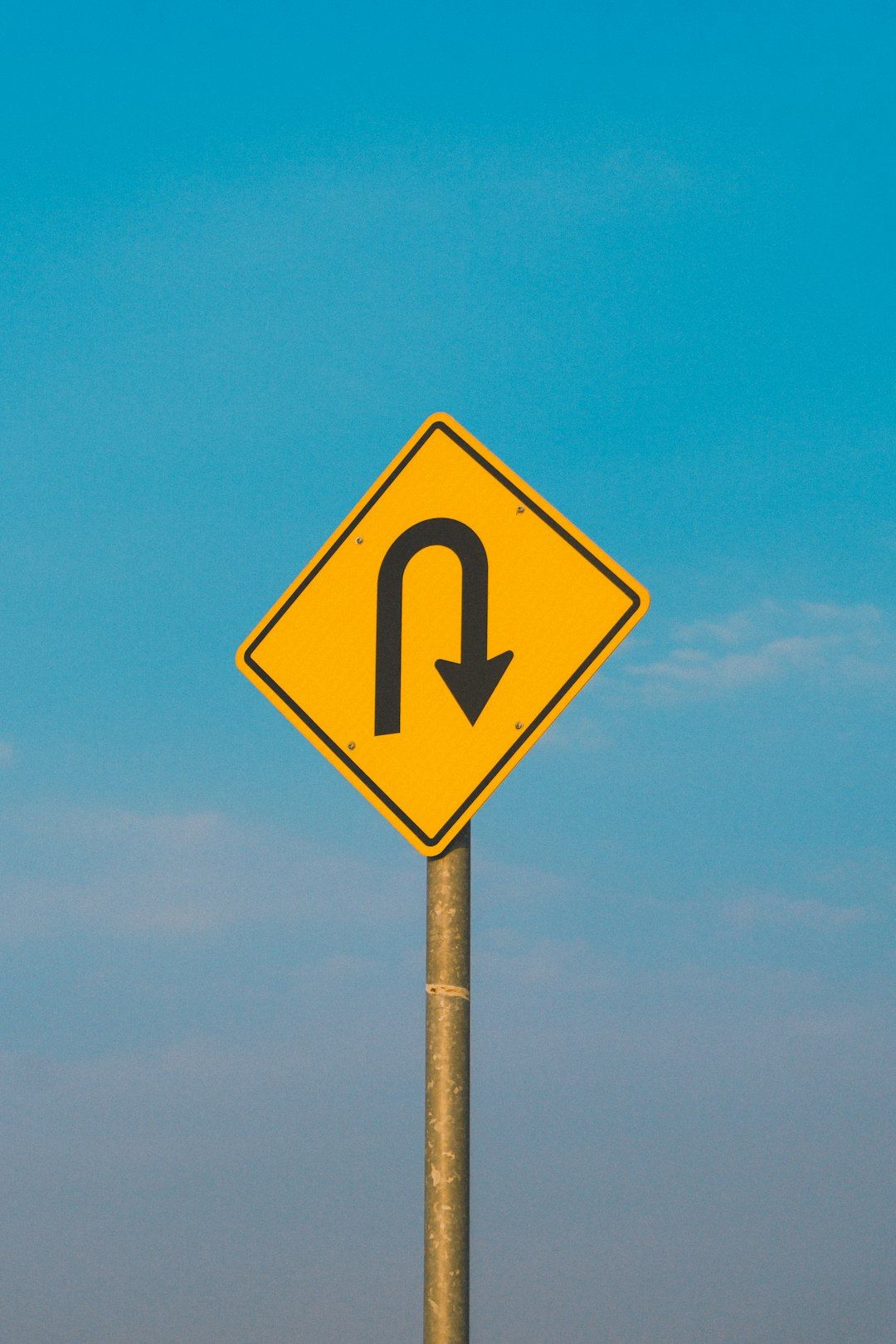 The image features a yellow diamond-shaped road sign indicating a U-turn. The background showcases a clear blue sky with minimal clouds.