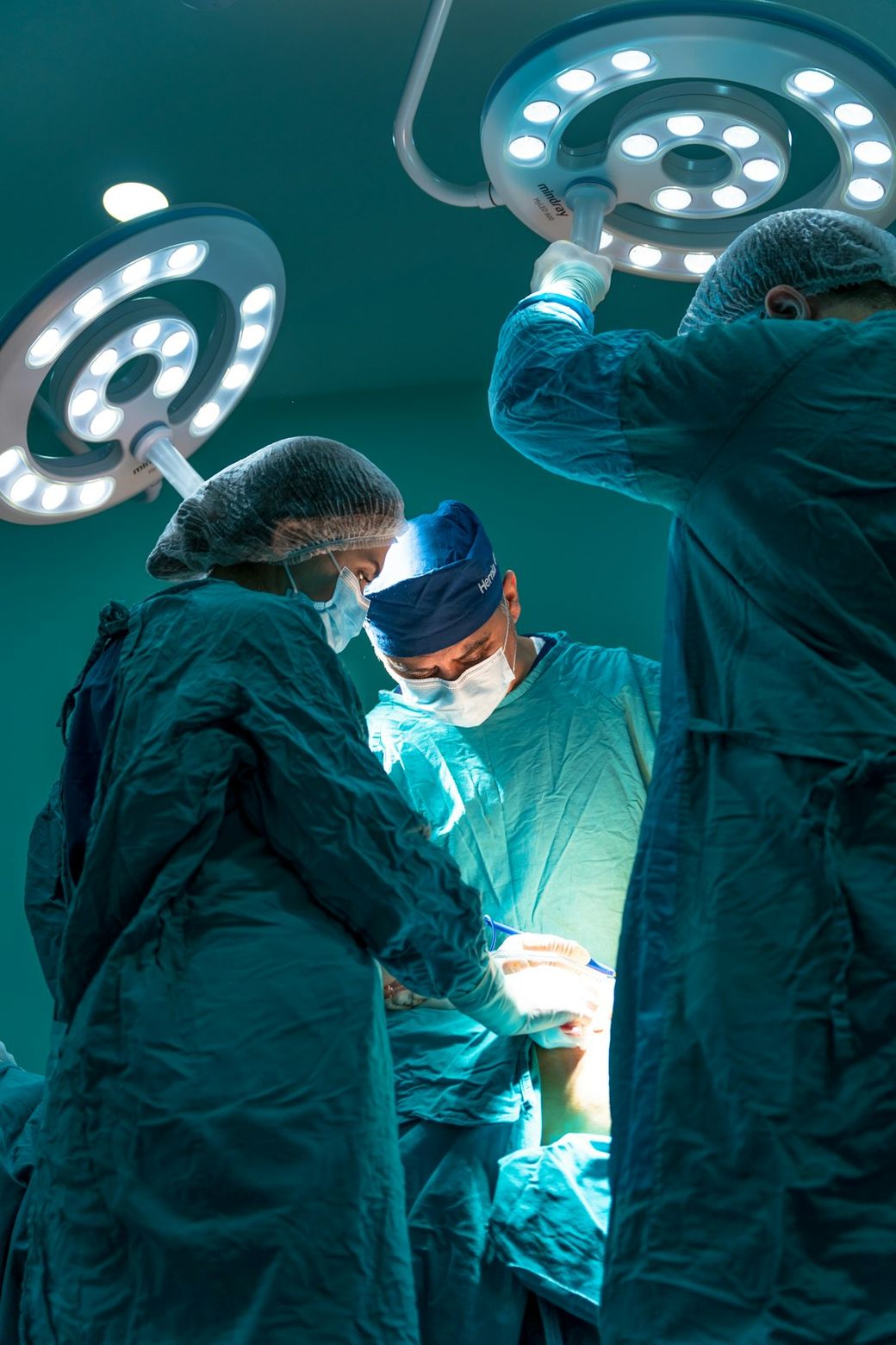 The image shows a surgical team in an operating room, focused on a procedure under bright surgical lights. The medical professionals are dressed in scrubs and masks, illustrating a moment of concentration and teamwork during surgery. — Credit: Photo by Akram Huseyn on Unsplash
