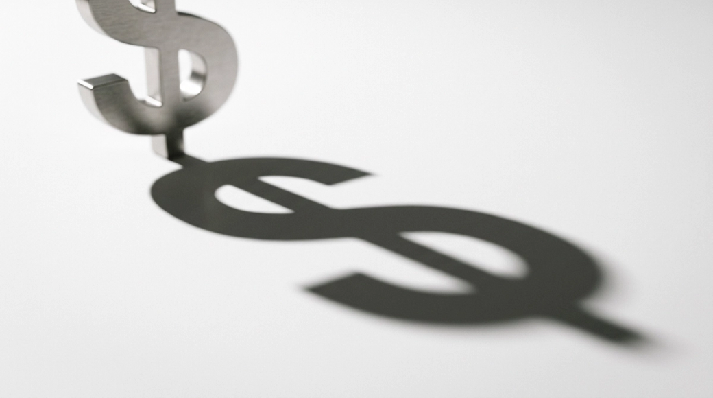 The image features a large dollar sign made of brushed steel, prominently displaying its shadow cast on a pristine white surface. The shadow, elongated and distorted, suggests a surreal representation of financial influence, highlighting the iconic symbol's power beyond its physical form.