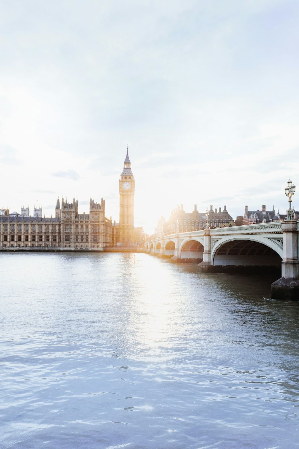 The image captures a scenic view of the River Thames with the iconic Big Ben and the Houses of Parliament in the background. The sunlight reflects off the water, creating a serene and picturesque atmosphere. — Credit: Photo by Hugo Sousa on Unsplash