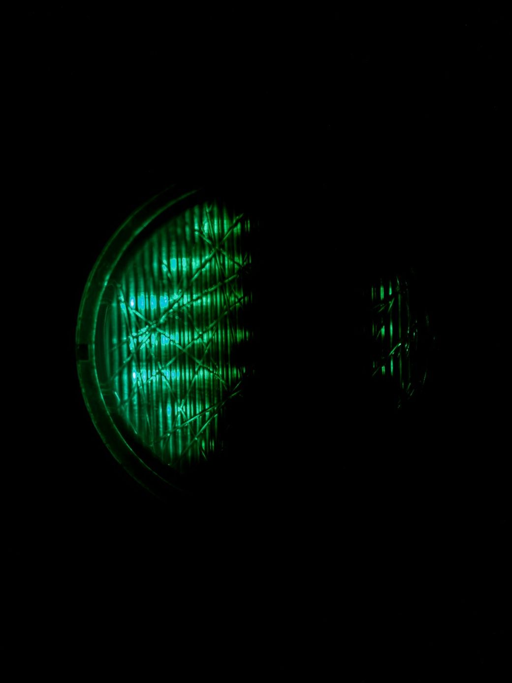 The image features a glowing green light against a dark background, resembling a traffic light or signaling device. The design of the light suggests a focus on visibility and indication. — Credit: Photo by Haberdoedas on Unsplash