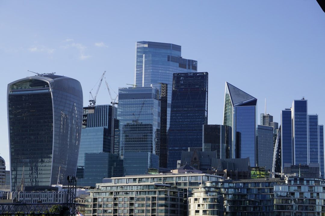 The image showcases a skyline of modern skyscrapers with reflective glass facades. Construction cranes suggest ongoing development in the area, highlighting urban growth and architectural innovation.