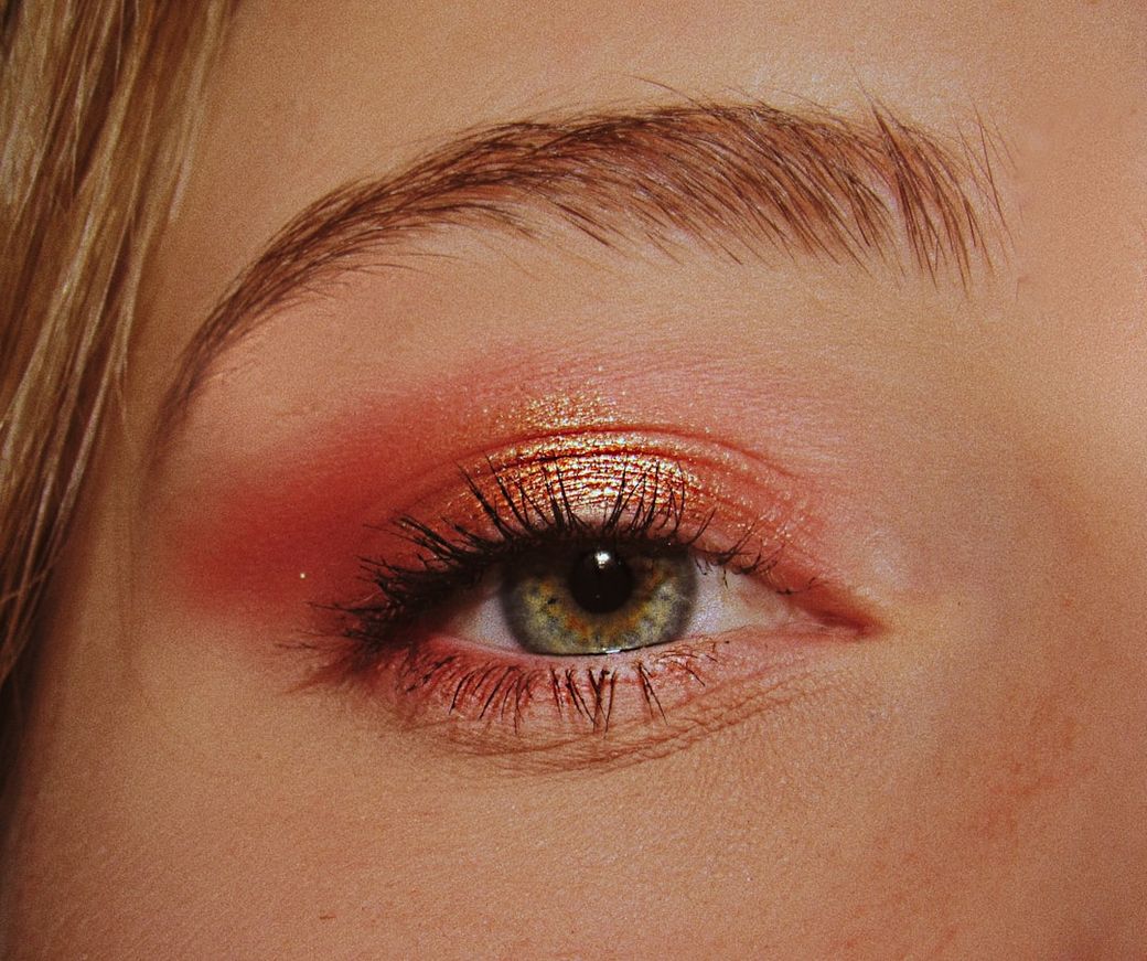 A close-up image of a human eye, showcasing vibrant eye makeup. The eyelid is adorned with shimmering shades of orange and peach, enhancing the eye's natural beauty. — Credit: Photo by yunona uritsky on Unsplash