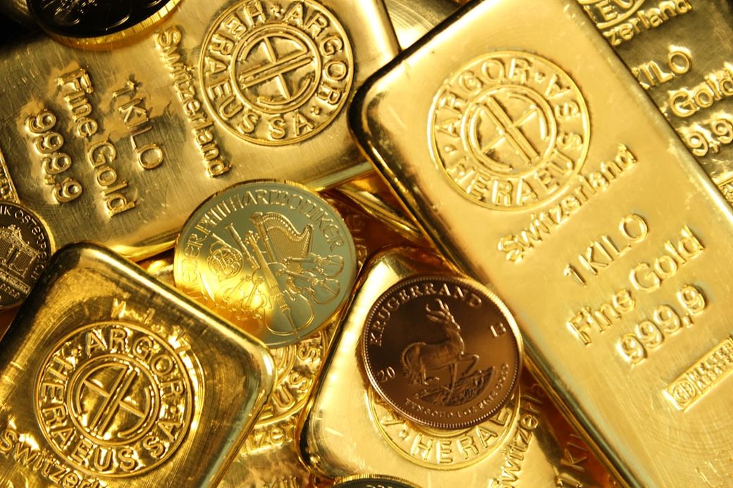 The image features a collection of gold bars and gold coins, showcasing their gleaming surfaces and distinct engravings. The bars are stacked and scattered, emphasizing the value of precious metals. — Credit: Photo by Zlaťáky.cz on Unsplash