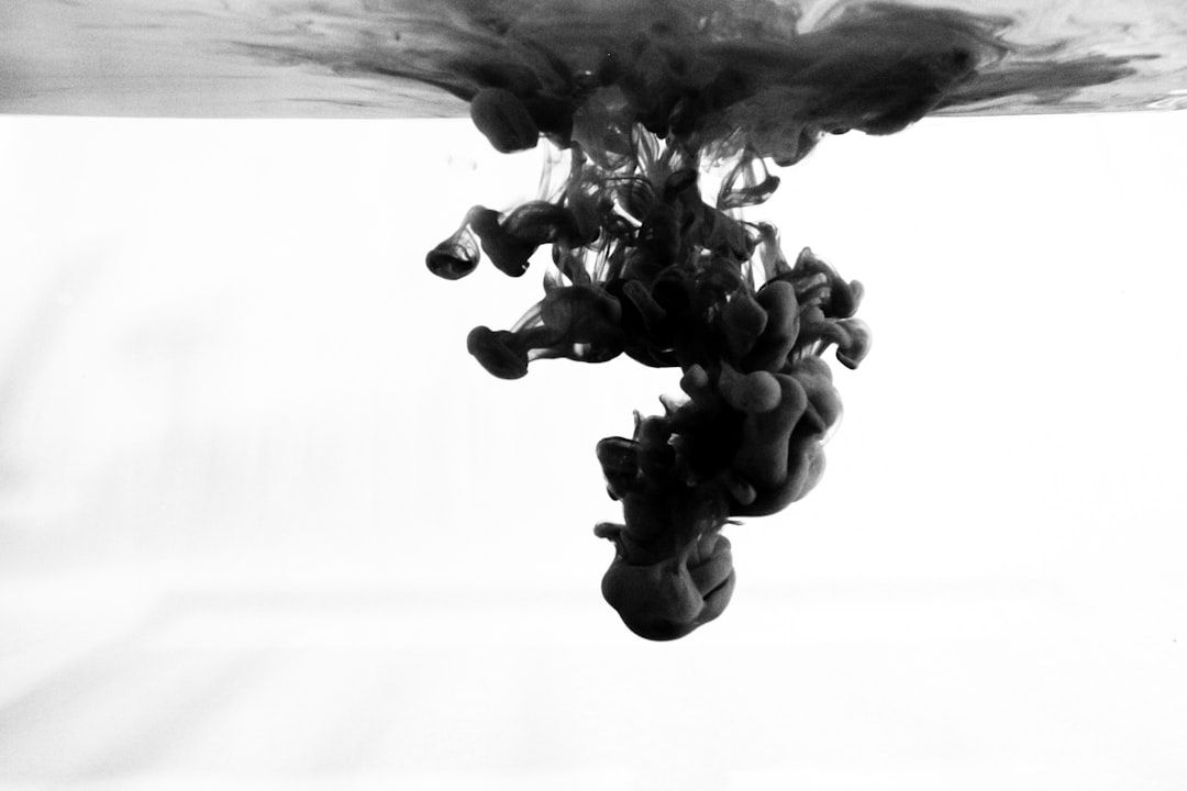 The image captures black ink swirling and dispersing underwater, creating dramatic patterns and shapes. The high contrast between the black fluid and the white background enhances the visual effect, giving it an artistic quality.