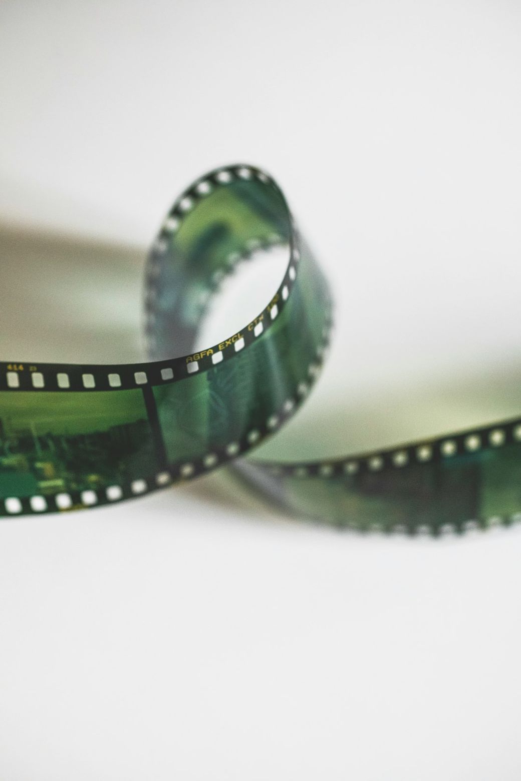 The image features a piece of film strip lying in a curled position, showcasing its perforated edges. The strip has a translucent green hue, indicating it is likely an analog film used for photography or cinema. — Credit: Photo by Markus Spiske on Unsplash