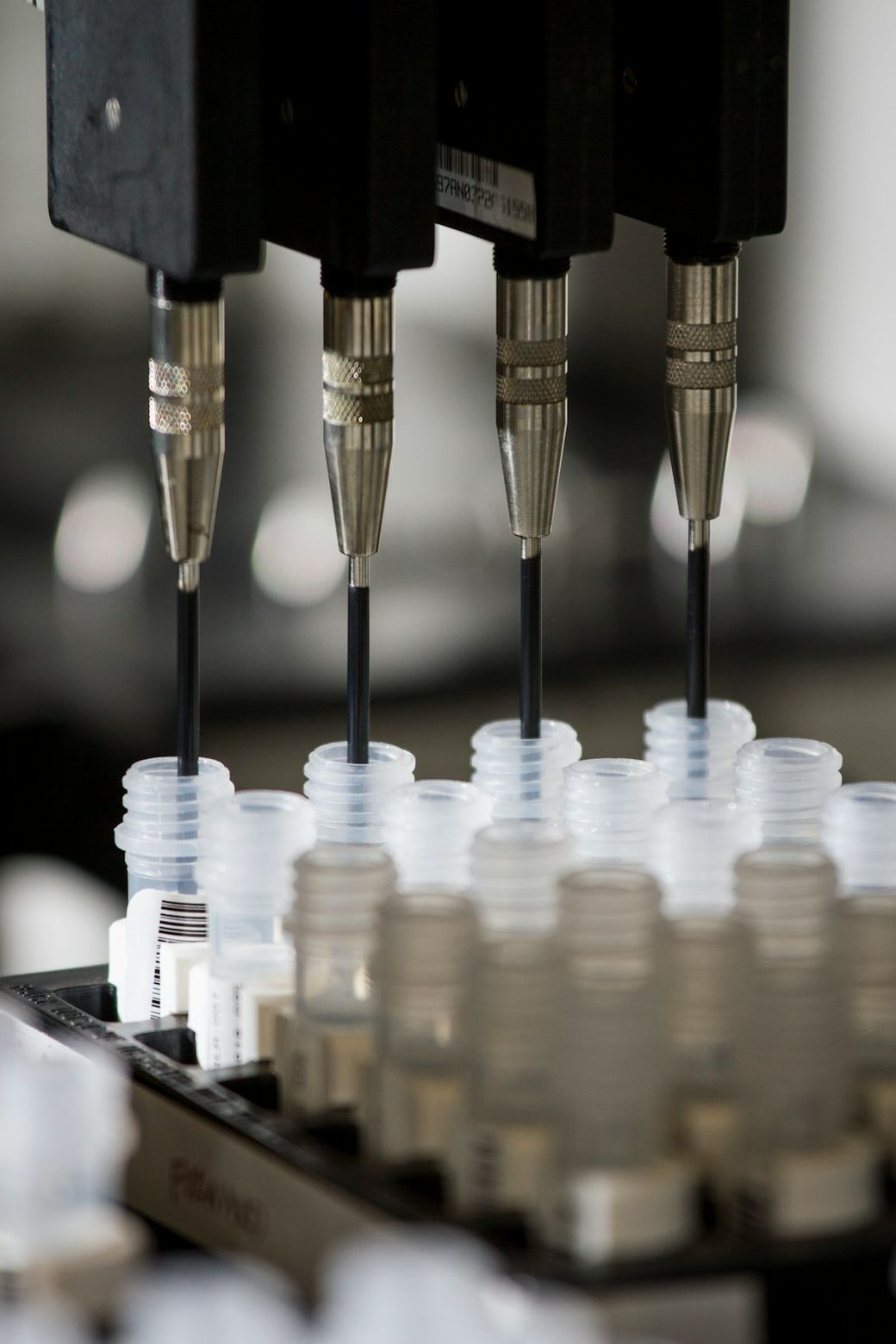 The image shows a close-up of a laboratory apparatus that is equipped with multiple precision dispensing tips. These tips are positioned above a tray filled with sample vials, suggesting a process related to automated liquid handling or chemical analysis. — Credit: Photo by National Cancer Institute on Unsplash