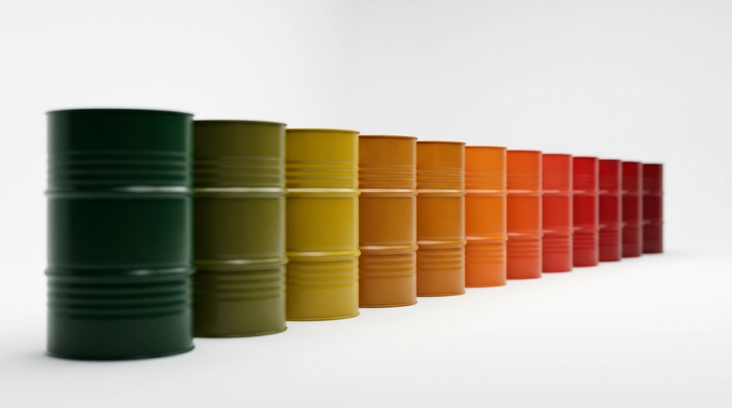 The image showcases a row of identical oil drums arranged in a linear fashion, transitioning from deep green at the front through amber to vivid red at the back. This colour gradient creates a visual representation of price movement and market sentiment, suggesting a spectrum from profit to loss against a clean white background.