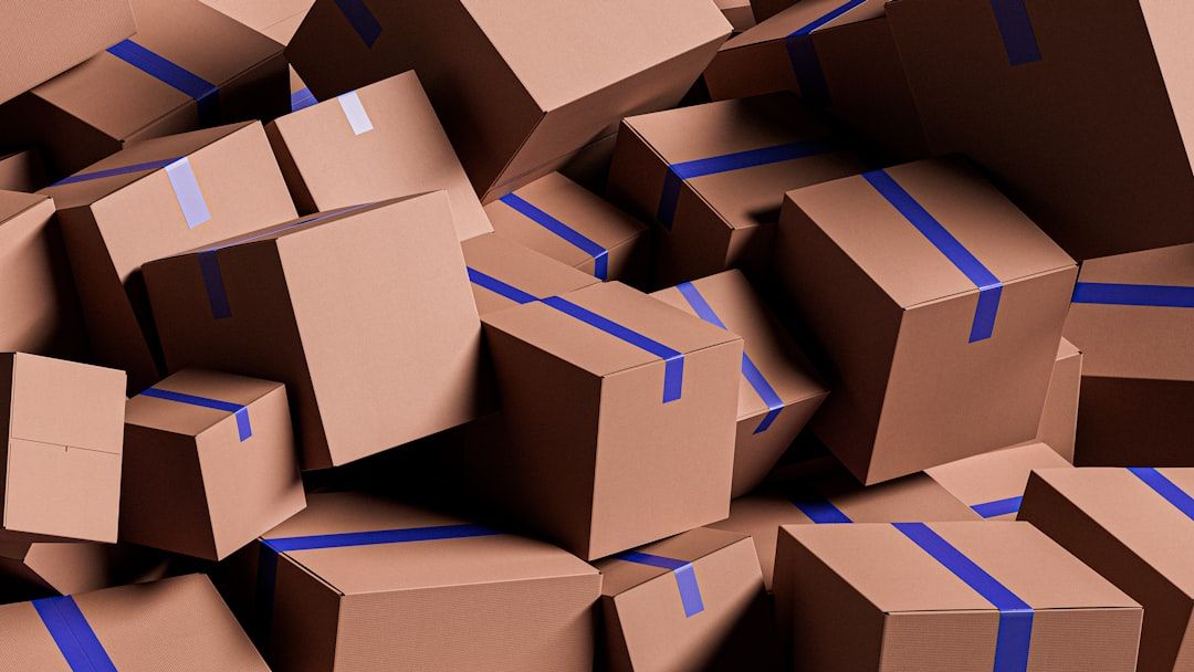 The image shows a large pile of brown cardboard boxes, featuring blue tape, stacked haphazardly. The boxes vary in size and are densely packed together, creating a chaotic yet organized appearance.