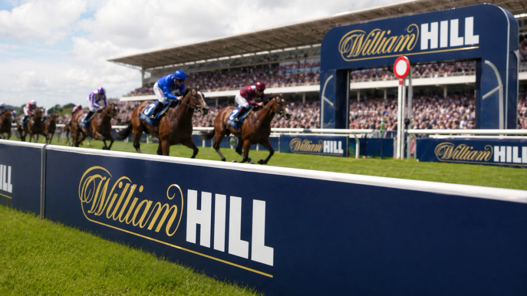 A horse race taken at a large outdoor event, with multiple horses in action as they race toward the finish line. The William Hill branding is prominently displayed in the foreground, indicating sponsorship of the event.