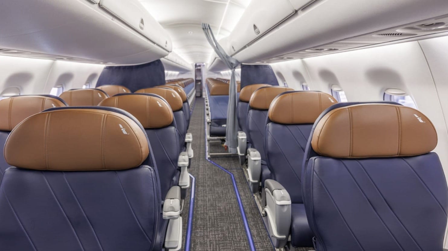The image showcases the interior of an aircraft, featuring a row of passenger seats with brown and navy blue upholstery. The aisle is visible, emphasizing the spacious layout and design of the seating area.