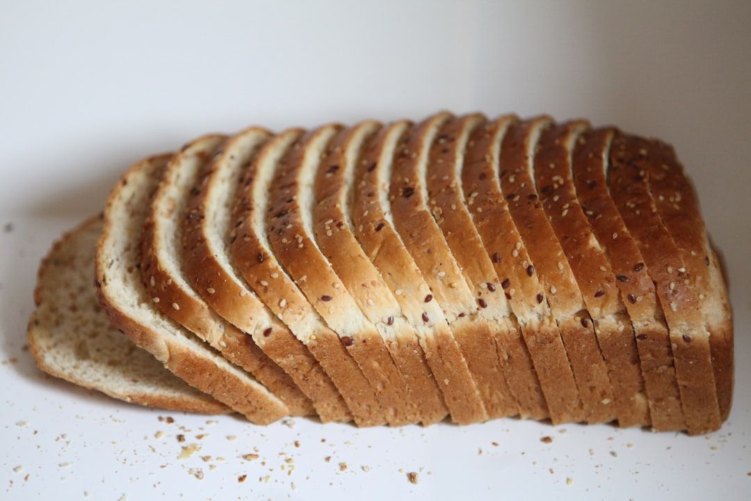 The image features a neatly sliced loaf of bread arranged on a plain background. The sliced bread showcases a golden-brown crust with bits of seeds visible throughout.