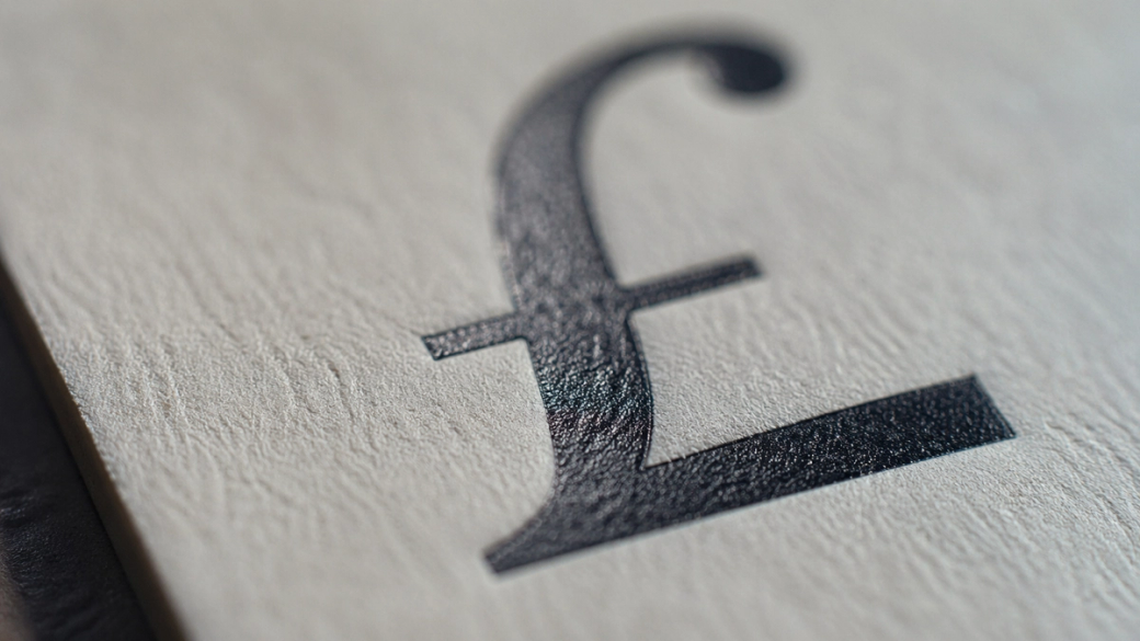 A close-up image of a textured surface featuring the symbol for the British Pound (£). The focus highlights the intricate details of the symbol, showcasing its design.