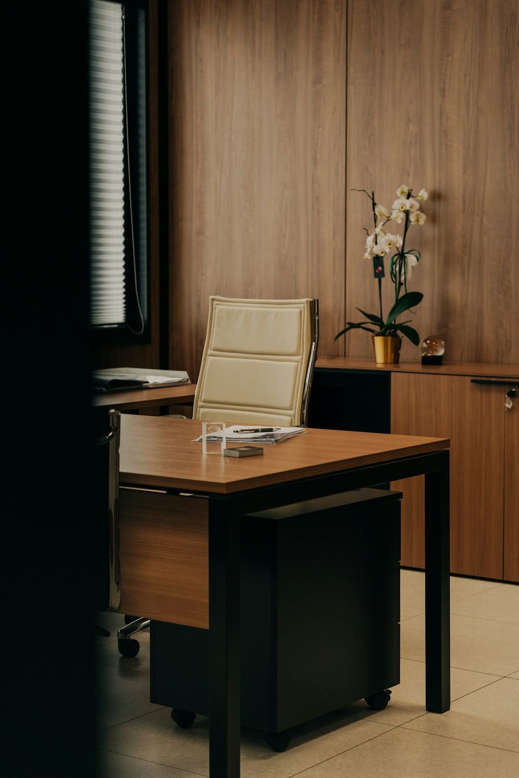 A modern office space featuring a wooden desk and a stylish office chair. The room is adorned with a potted orchid and has a warm, inviting atmosphere. — Credit: Photo by Francesco Liotti on Unsplash