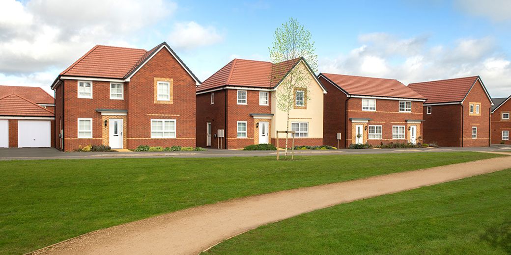 The image features a row of newly built brick houses arranged along a manicured lawn with a pathway. The houses have pitched roofs and are set against a partly cloudy sky, indicating a suburban residential area.