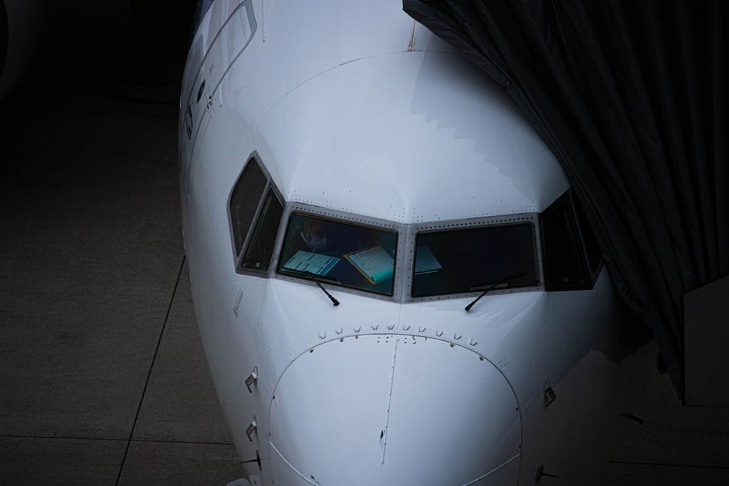 The image features the cockpit of a commercial aircraft, showcasing the windshield and the surrounding fuselage. The view is taken from an angle that highlights the folded wing and the surface of the tarmac. — Credit: Photo by Ryuno on Unsplash