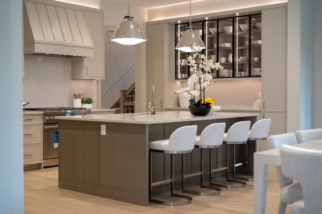 The image showcases a modern kitchen with a spacious island and bar stools. The design features neutral tones and elegant fixtures, creating a contemporary and inviting atmosphere. — Credit: Photo by Franco Debartolo on Unsplash